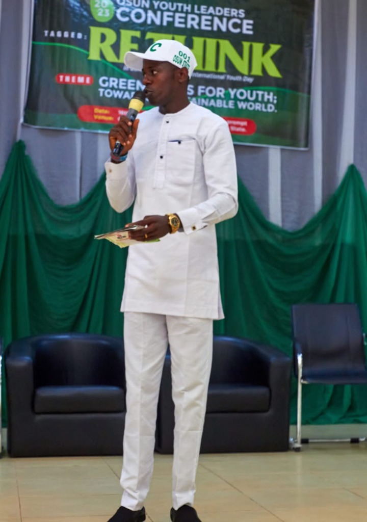 OmoAkin standing on stage in white native attire holding microphone addressing the 2023 Osun Youth Leaders Conference tagged Rethink